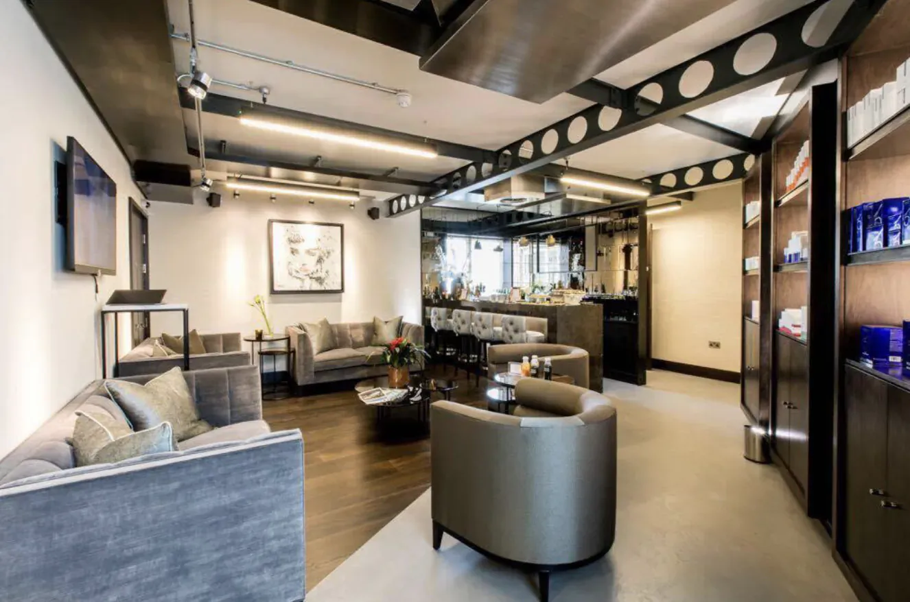 Modern Mallucci aesthetic clinic interior with gray sofas, bar area, art, and skincare products on shelves.