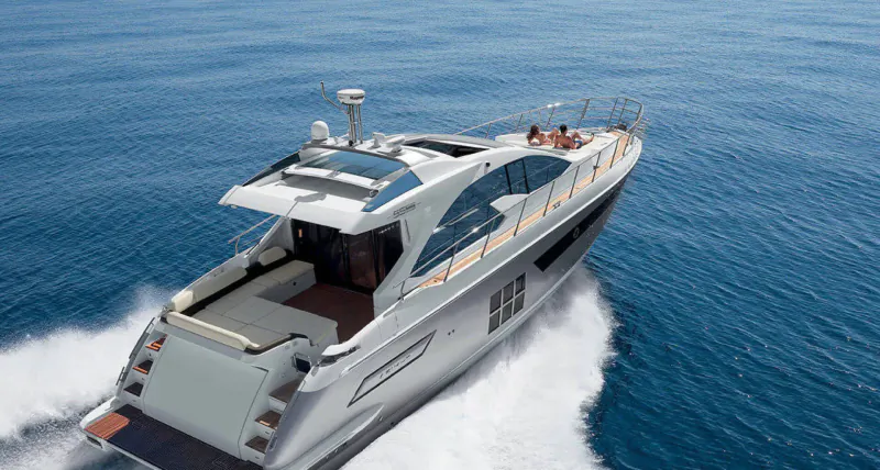 Aerial view of sleek white luxury yacht speeding on blue ocean, creating white wake, people on deck.