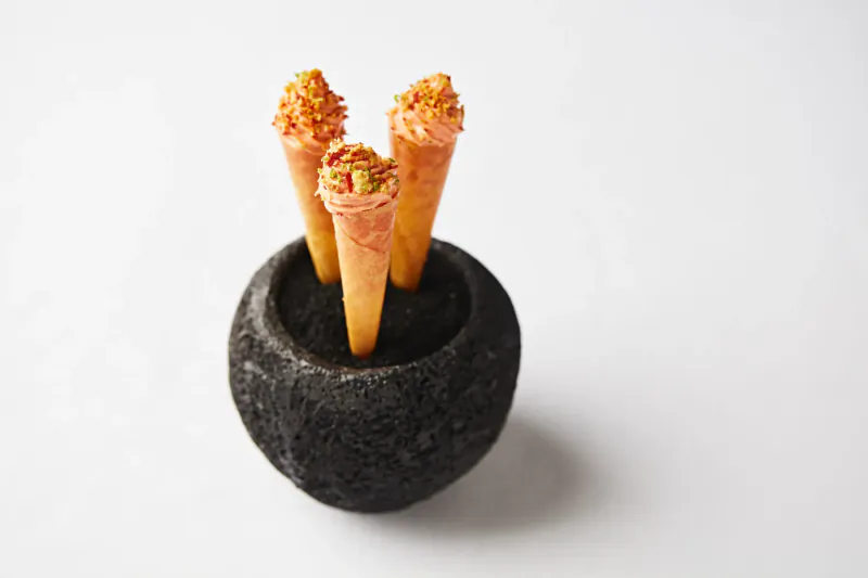 Three orange waffle cones topped with pink cream and pistachios in a black stone holder