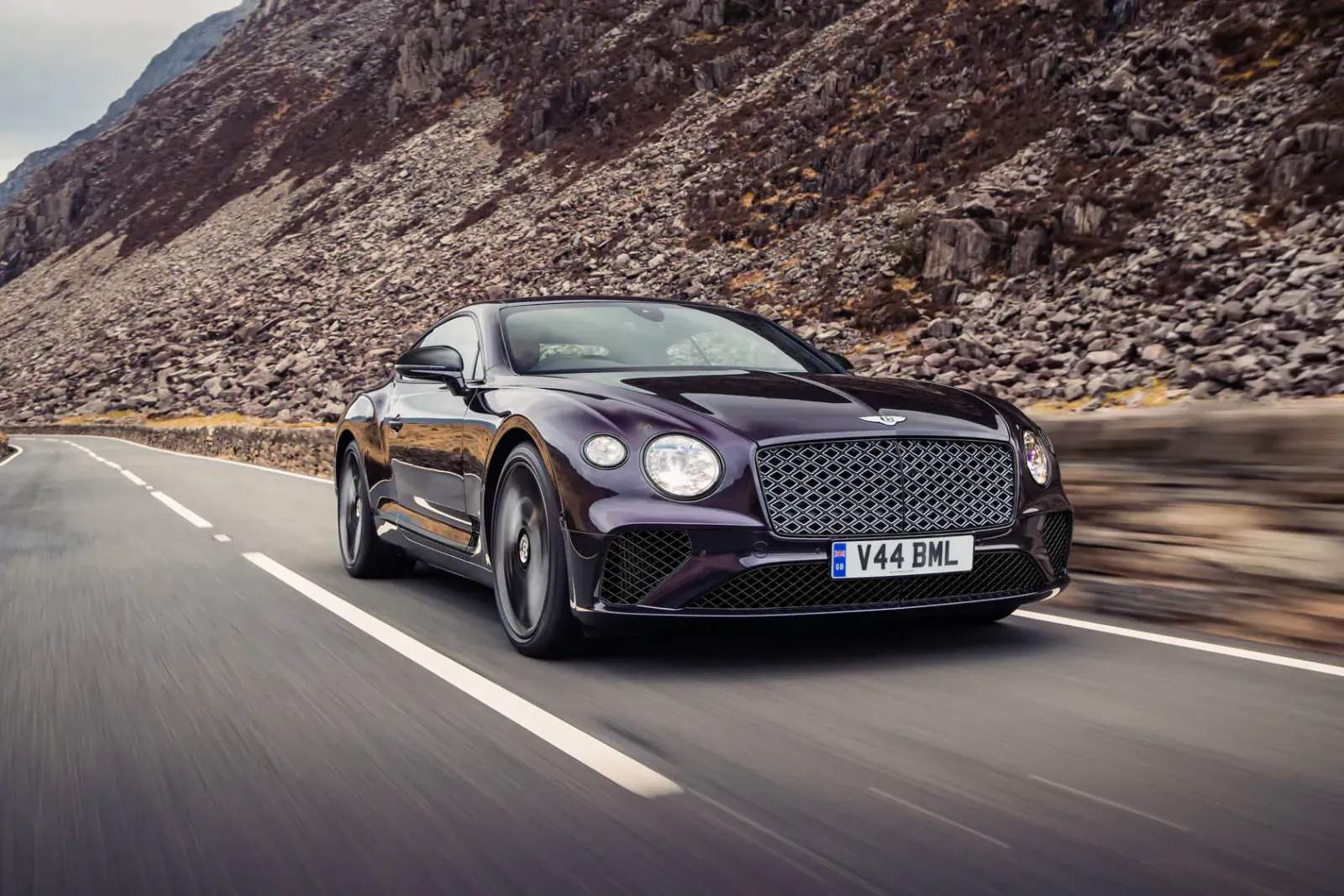 Purple Bentley GT Mulliner Blackline speeding on mountain road, license plate V4 GTML