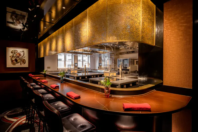 Elegant Cocochine restaurant interior with curved wooden sushi bar, red napkins, gold ceiling panels, and art.