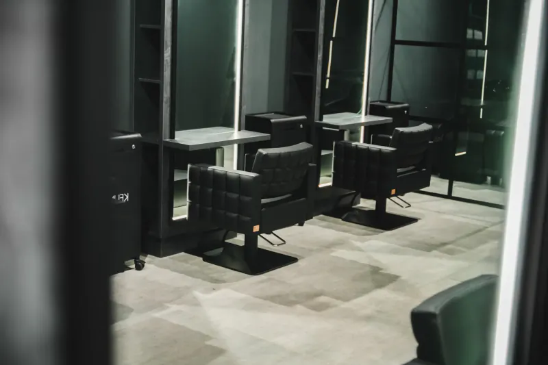 Modern empty hair salon interior with black leather stylist chairs, mirrors, and shelves.