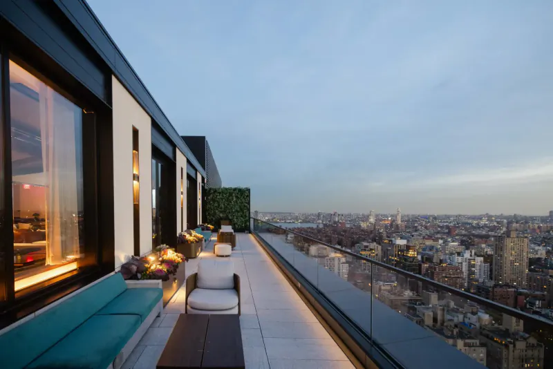 Modern rooftop terrace with teal sofa, white chairs, and city skyline view at dusk in New York