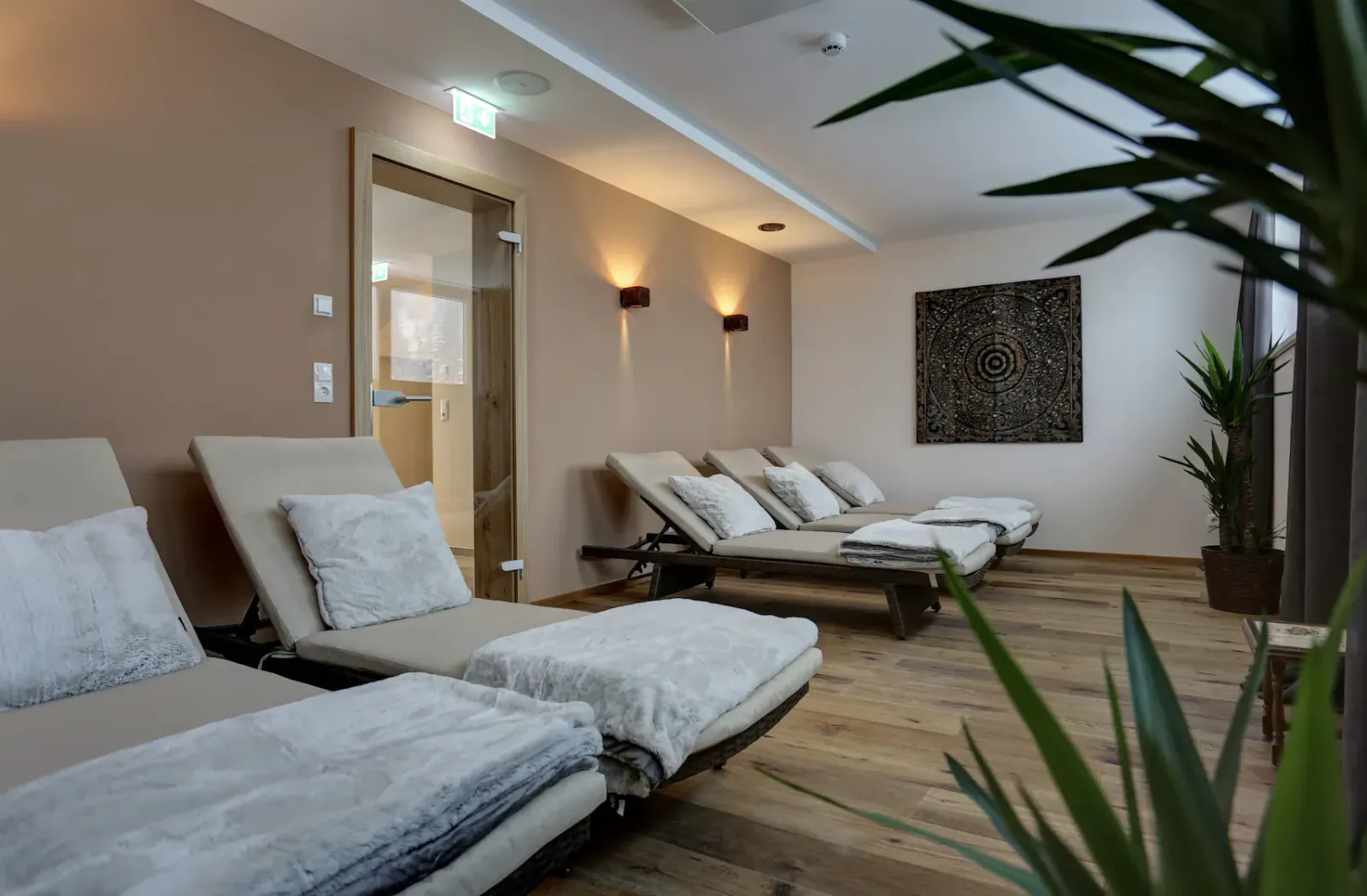 Luxury spa lounge with plush beige loungers, towels, plants, and sauna door in Hotel Kösslerhof.