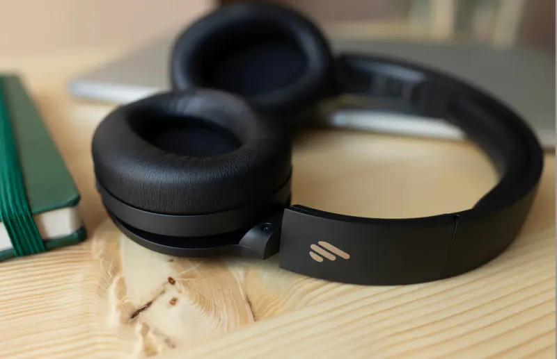 Black Edifier W820NB headphones with 'Edifier' logo on a wooden table beside green notebook and silver laptop