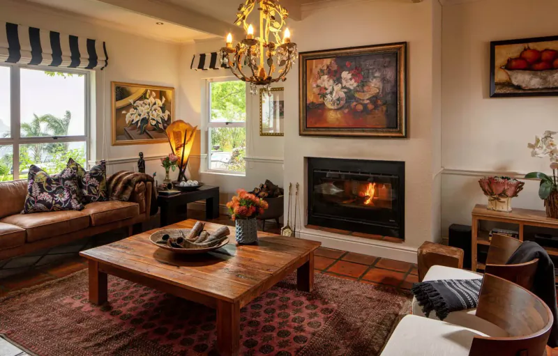 Cozy living room in Spanish Farm Guest Lodge with lit fireplace, wooden coffee table, leather sofa, chandelier, and art.