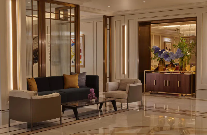 Elegant hotel gallery lounge with navy sofa, armchairs, glass coffee table, purple flowers, and modern decor.