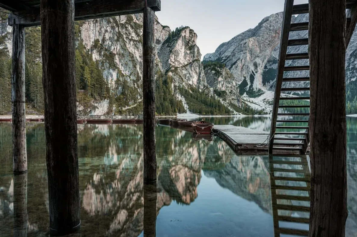 Wooden pier with ladder extending over reflective lake, framed by jagged mountains at Tre Cime di Lavaredo