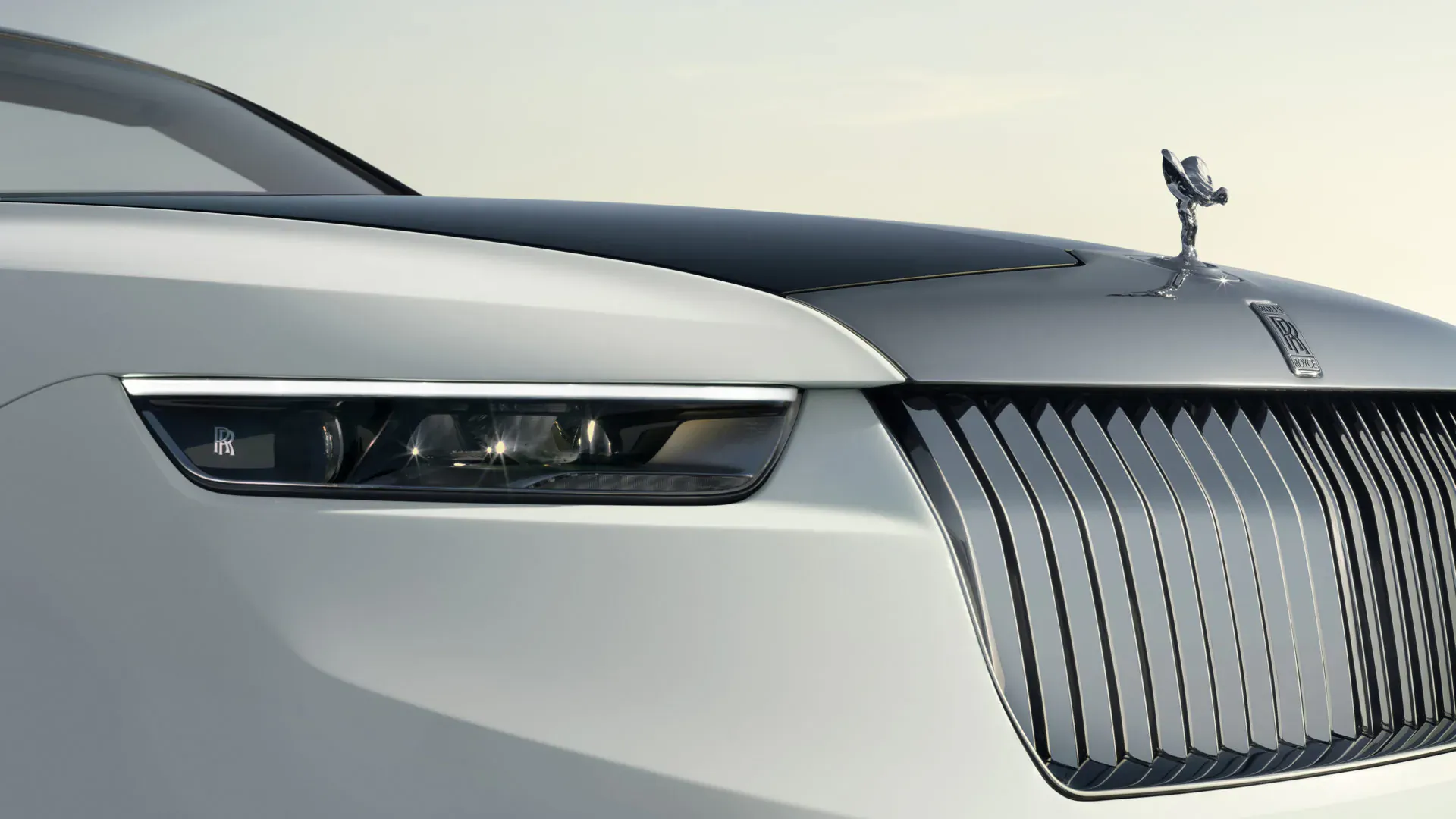 Rolls-Royce Arcadia Droptail front view with sleek white body, black hood, illuminated headlights, Spirit of Ecstasy hood ornament, and prominent grille.