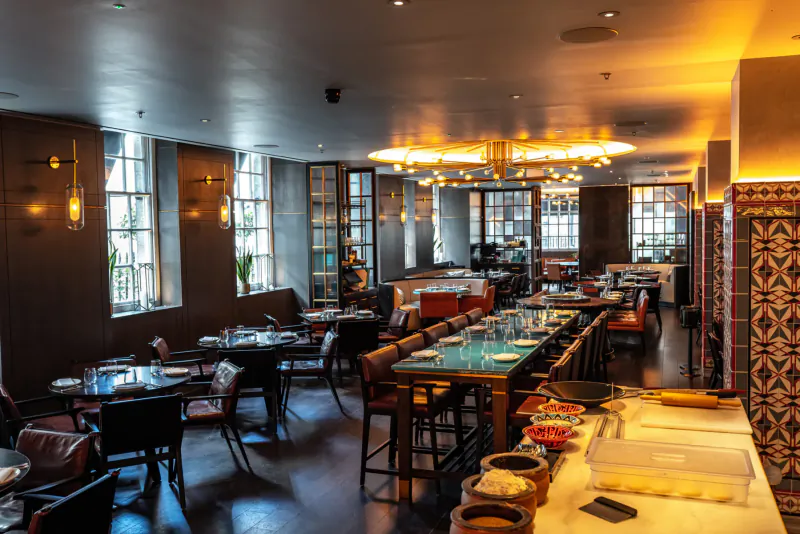 Elegant Rüya London dining room with wooden tables, red chairs, warm lighting, large windows, and tiled walls