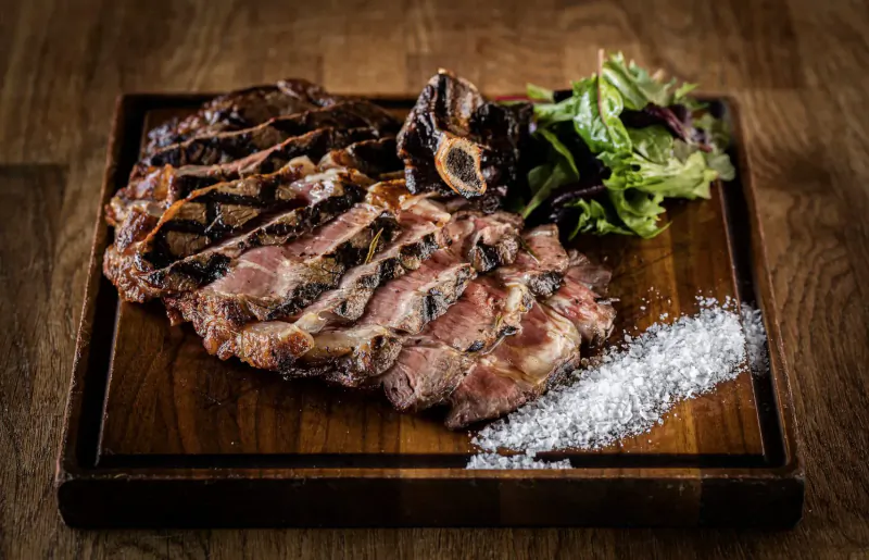 Sliced grilled bone-in short ribs with greens and sea salt on wooden board