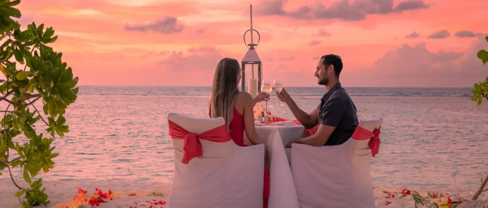 Romantic couple toasting wine at candlelit beach dinner table during sunset at Hideaway Beach Resort