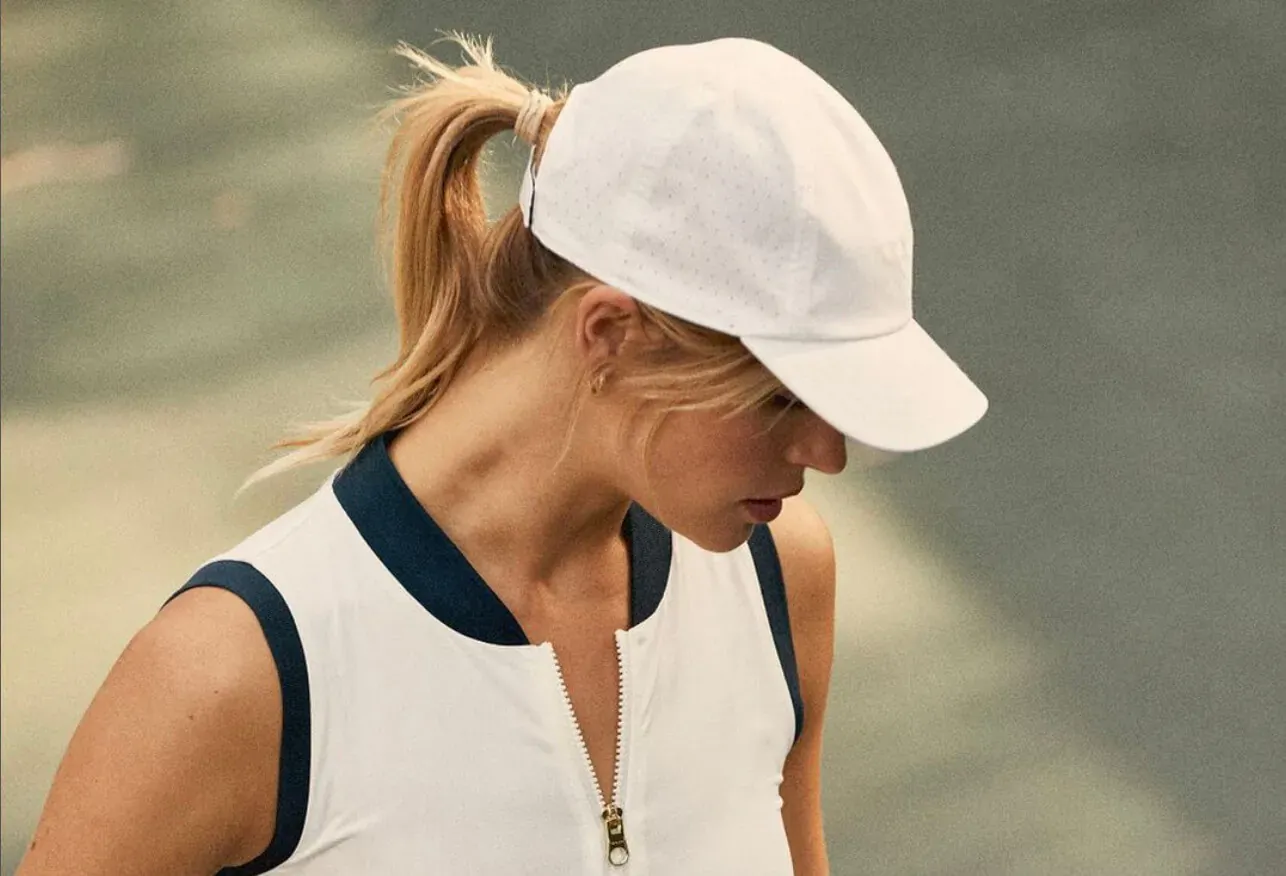 Laura Bailey in white cap and navy-trimmed tank top from Varley tennis collection, outdoors