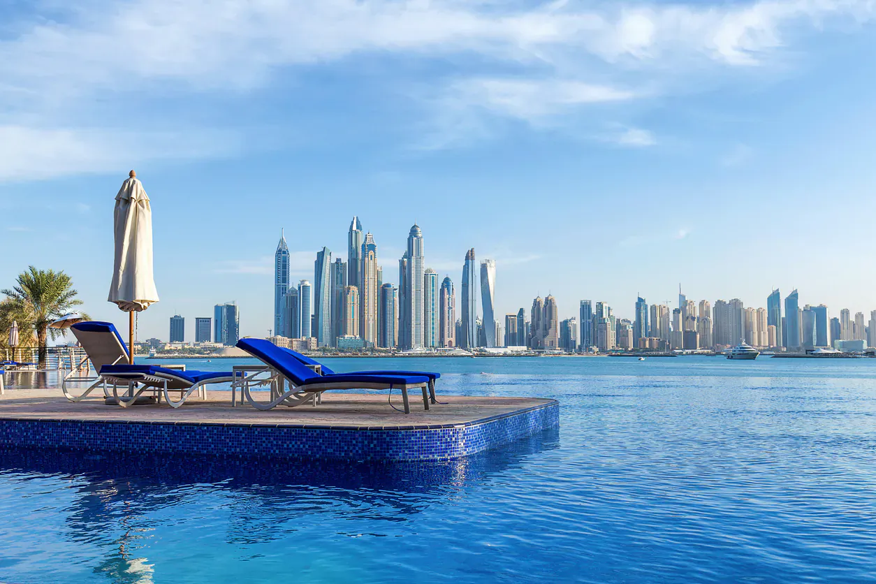 Luxury poolside lounge chairs and umbrellas on tiled deck overlooking Dubai skyline and blue water