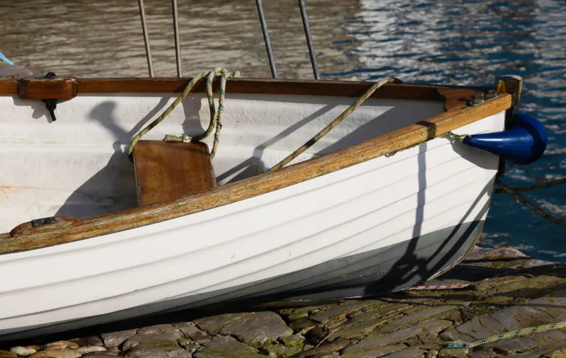 White wooden rowboat with blue fender and ropes moored at stone dock on calm water