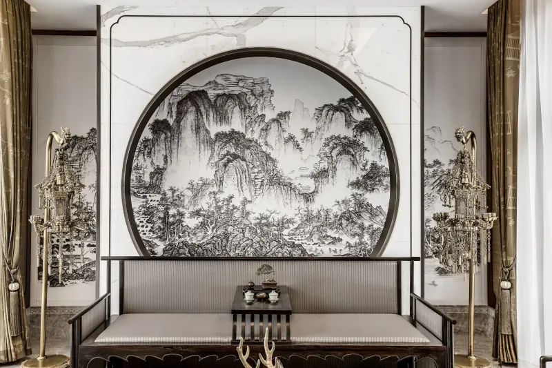 Elegant room with large central ink wash painting of misty mountains in round marble frame, flanked by gold candelabras and cushioned bench.