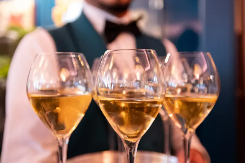 Server holding tray of three glasses of golden white wine in elegant setting