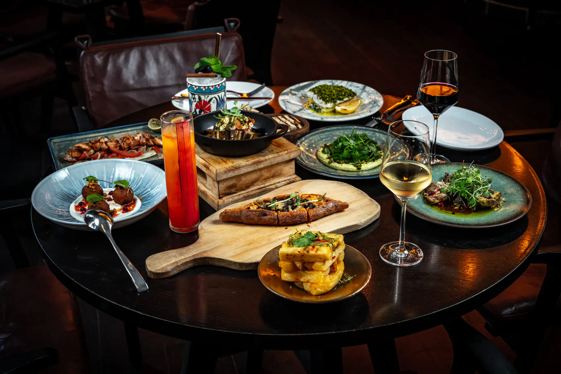 Assortment of Anatolian dishes on a dark round table in upscale restaurant with wine glasses