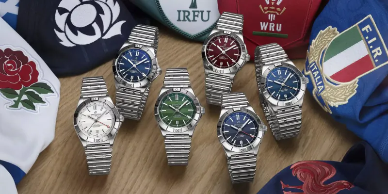 Selection of luxury Breitling watches in silver, blue, green, red on wood table with rugby union flags: IRFU, WRU, England, Scotland, Italy.