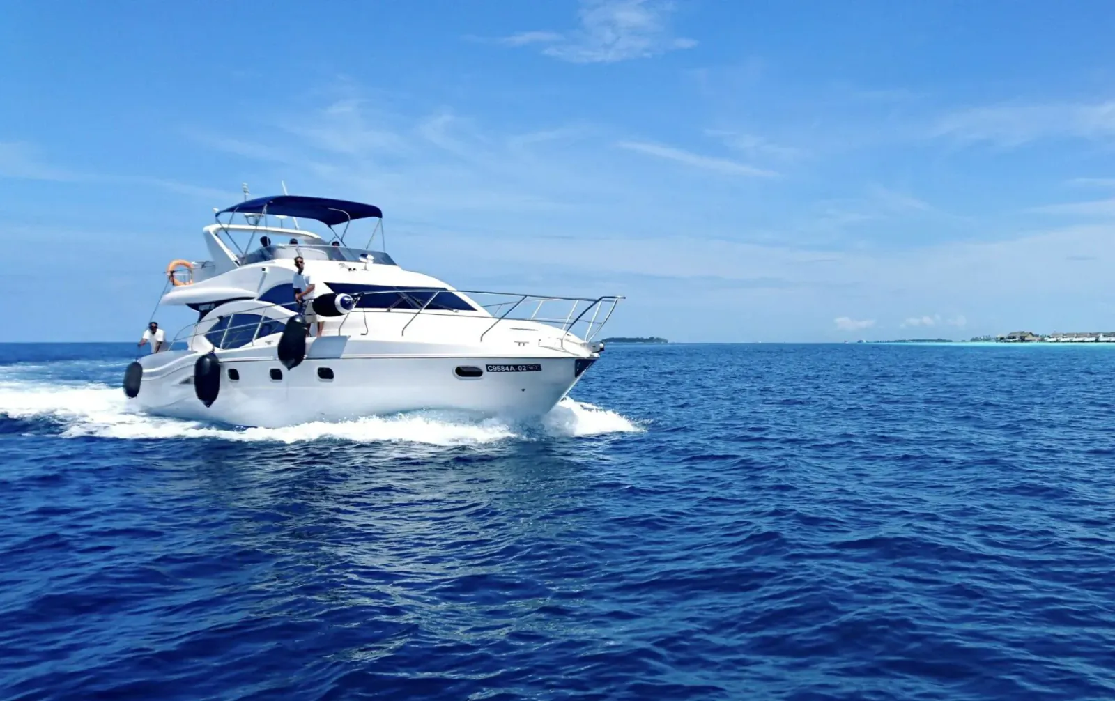 White luxury yacht speeding through turquoise ocean waters under blue sky with distant island.