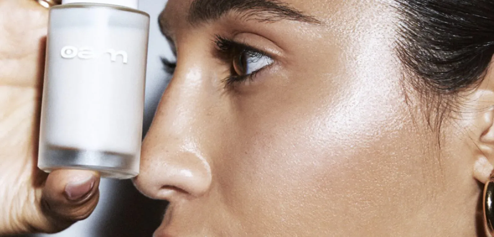 Close-up of woman's eye as hand applies EYEAM serum dropper for sensitive skin, with gold hoop earring.