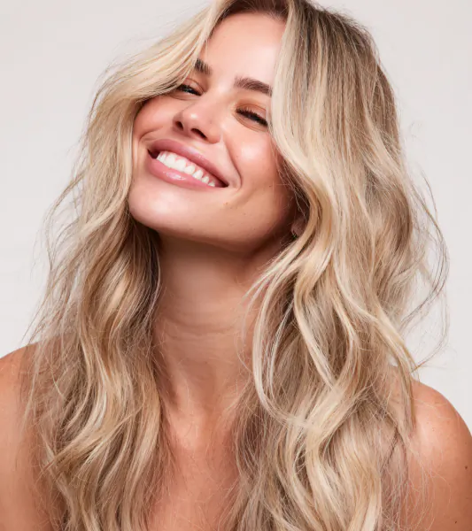 Blonde woman with wavy hair smiling joyfully, close-up portrait for Edward James London hair salon