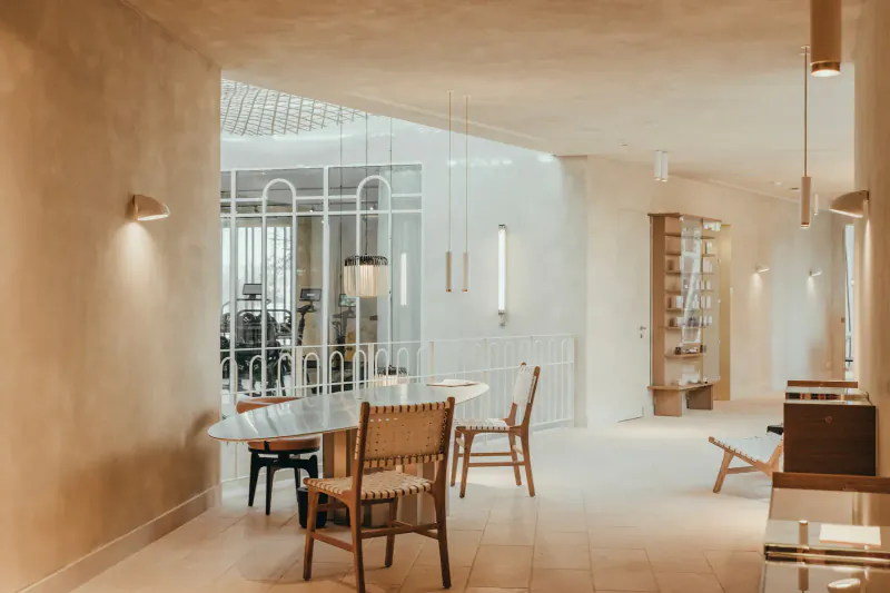 Spacious, light-filled spa gallery at Maslina Resort with modern wooden chairs around oval table, arched glass walls, and pendant lights