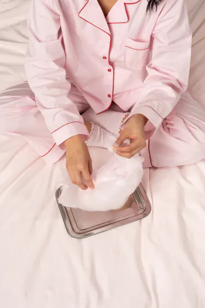 Woman in pink pajamas sitting on bed, holding fluffy white Kapten & Son Cloud Club object