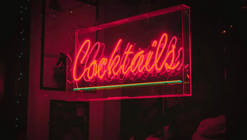 Glowing neon 'Cocktails' sign in red frame, dimly lit luxury bar setting.