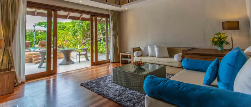 Spacious beach villa living room with blue sofas, open doors to tropical garden and infinity pool at Hideaway Beach Resort, Maldives