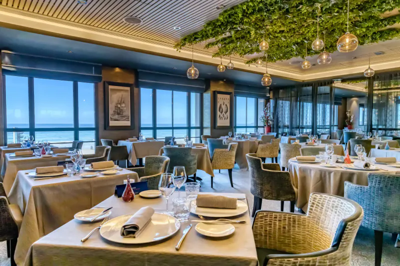 Elegant Nouveau Monde restaurant in Saint-Malo with ocean-view tables, green ceiling plants, pendant lights.