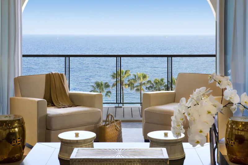 Luxurious hotel suite with beige armchairs, orchids, coffee table, and ocean balcony view at Cannes.