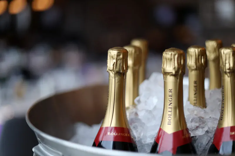 Close-up of Bollinger champagne bottles in ice-filled silver bucket, blurred festive background.