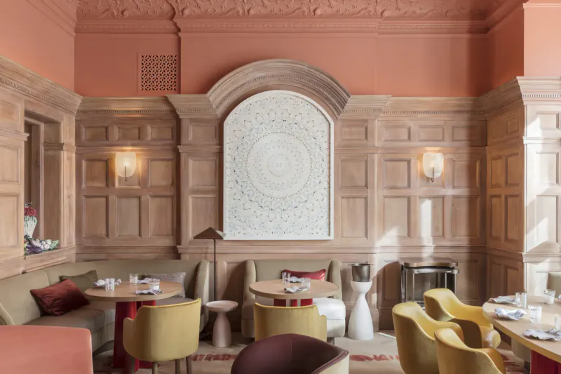 Elegant wood-panelled dining room at Hélène Darroze at The Connaught with mustard chairs, round tables, white mandala artwork, peach walls.