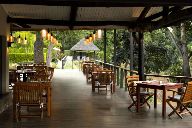 Spacious wooden veranda at The Norfolk Nairobi with empty tables, lanterns, and lush jungle view.