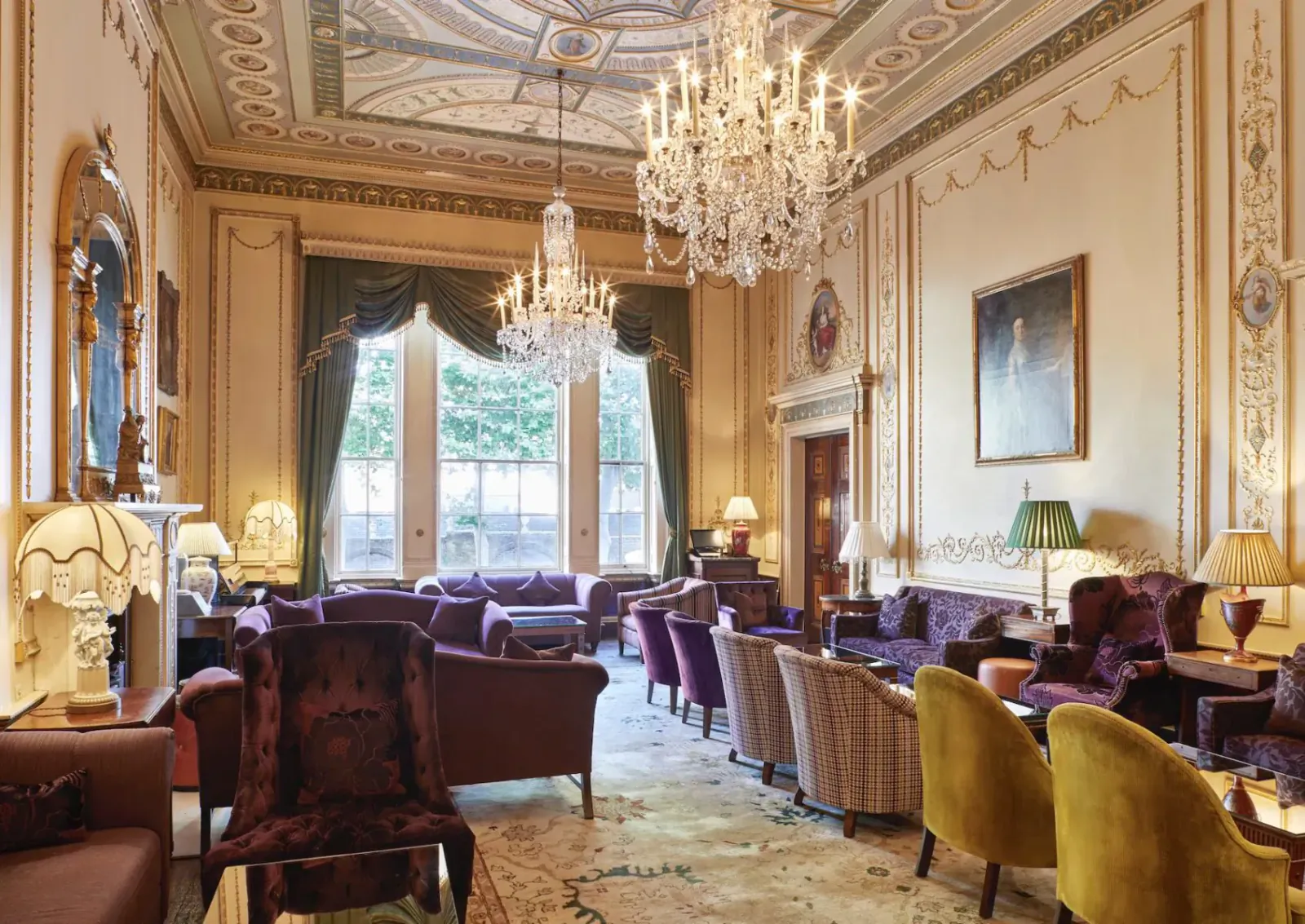 Elegant Home House lounge with ornate ceiling, chandeliers, plush purple armchairs, sofas, and large curtained windows.