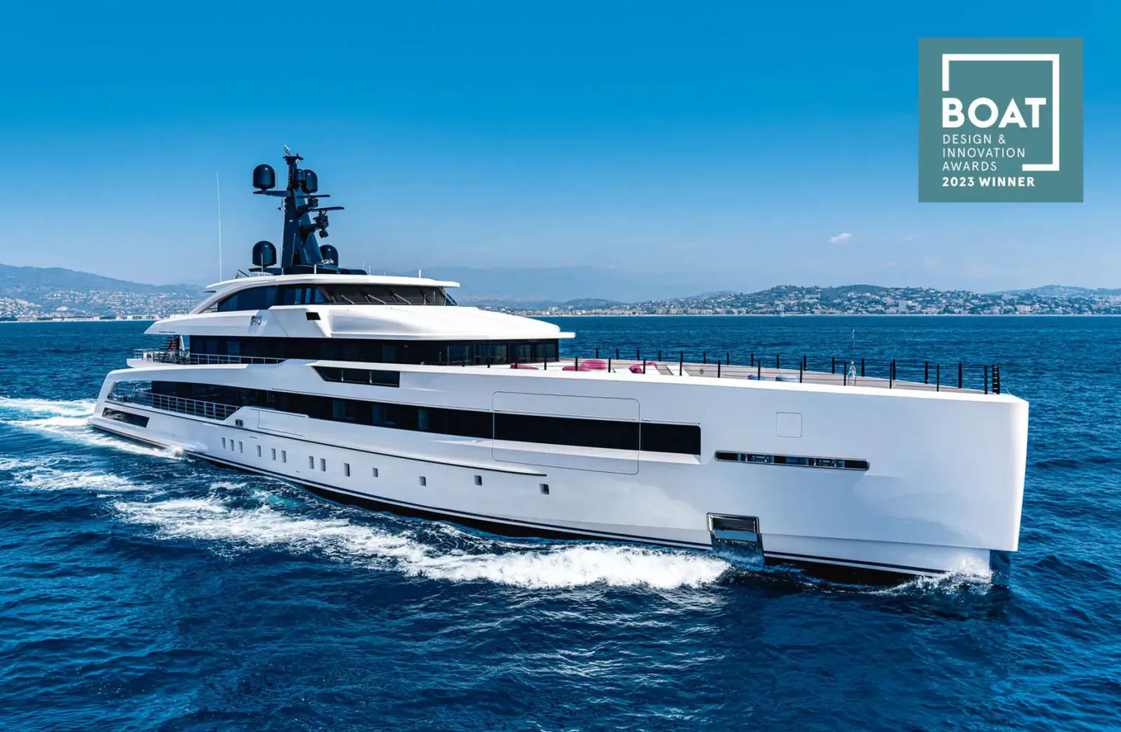 White luxury superyacht CRN M/Y RIO speeding on sea with mountains backdrop, BOAT logo overlay. 2023 Design & Innovation Awards winner.