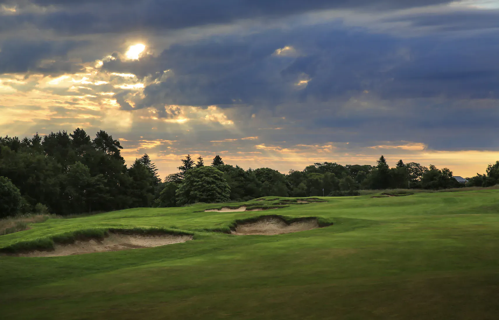 The Old Course at St Andrews: lush green fairway with bunkers, surrounded by trees under dramatic sunset clouds
