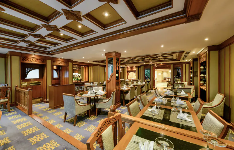 Elegant Nipa Thai restaurant interior with wooden beamed ceiling, ornate chairs, set tables, and warm lighting.