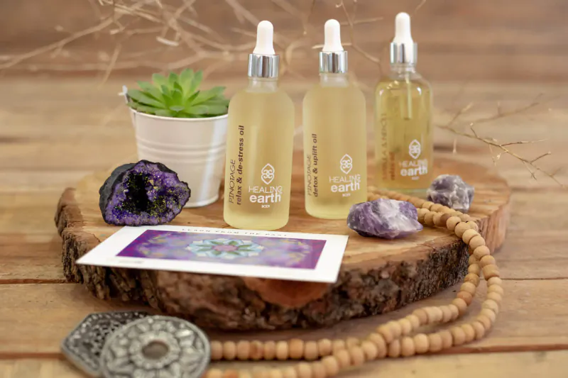 Three 'Earth' dropper bottles of golden oil on wooden slice with amethyst, succulent, tarot card, beads
