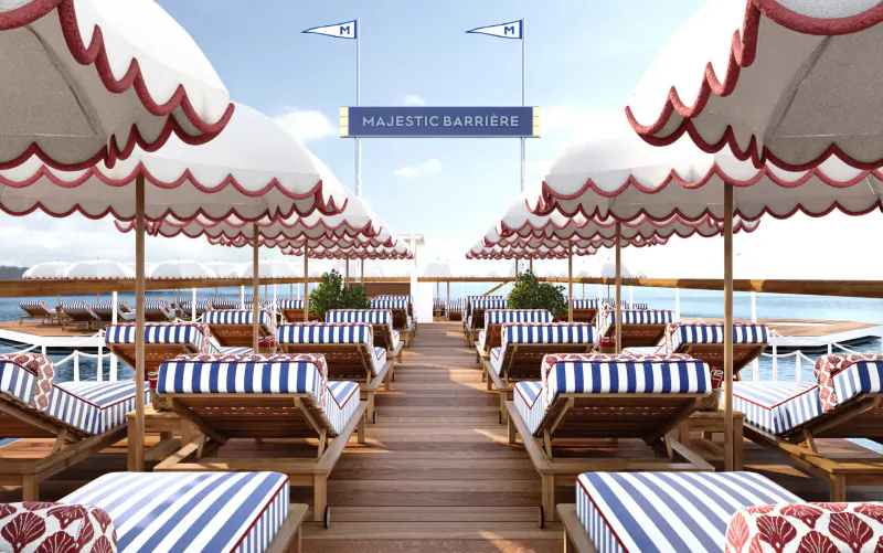 Majestic Barrière deck with white umbrellas, striped lounge chairs on wooden pier by sea, 'Majestic Barrière' sign.