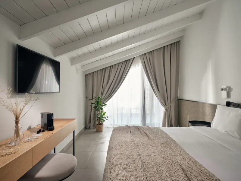 Luxurious hotel room at Contessina Hotel Zakynthos with wooden beamed ceiling, king bed, TV, plants, and sea view balcony.