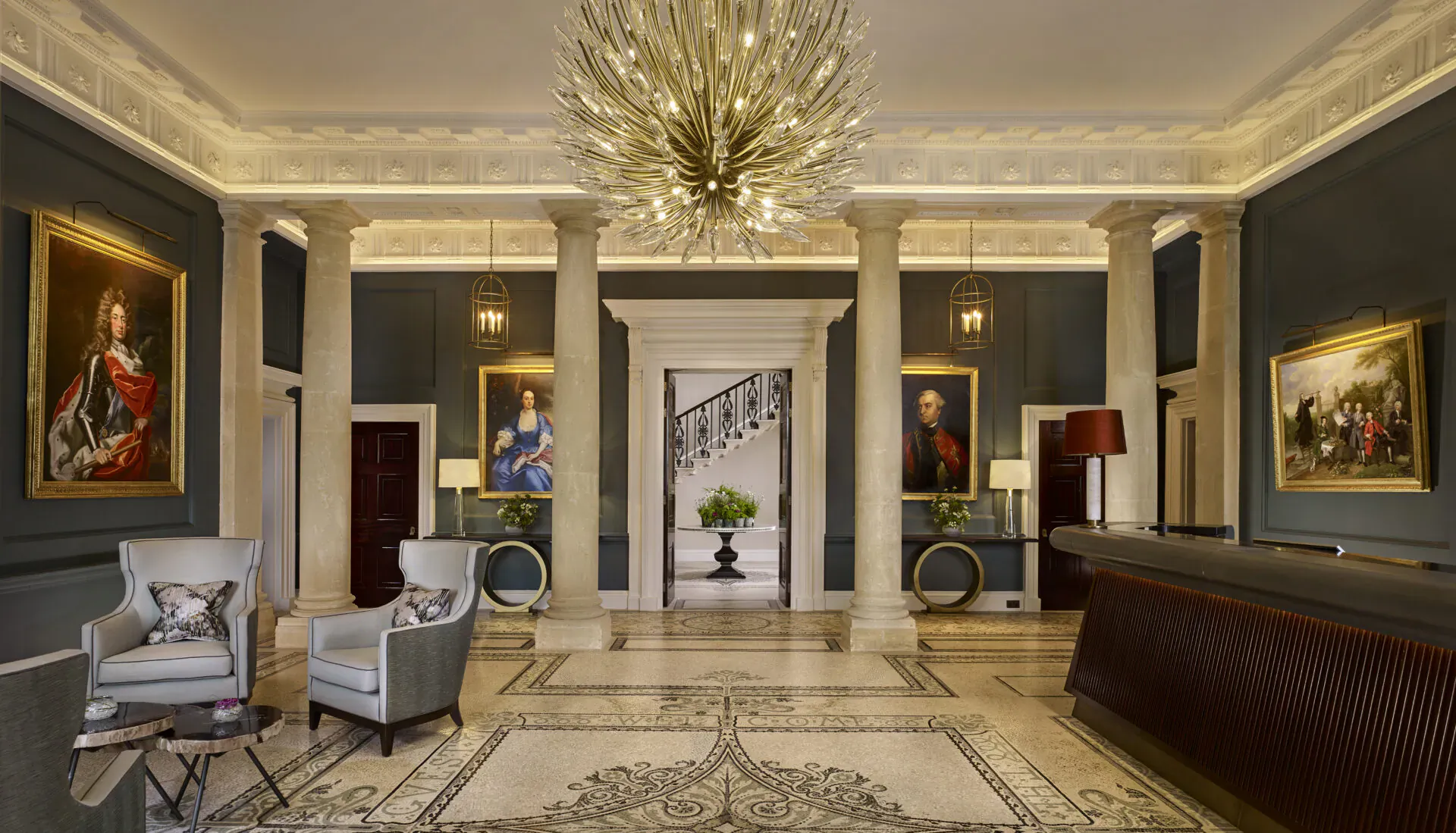 Opulent grand lobby of The Langley luxury hotel with chandelier, columns, gilded portraits, armchairs, and reception desk.