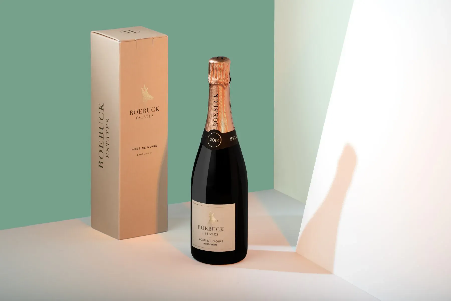 Roebuck Estates Blanc de Blancs champagne bottle beside its box on white surface with green backdrop