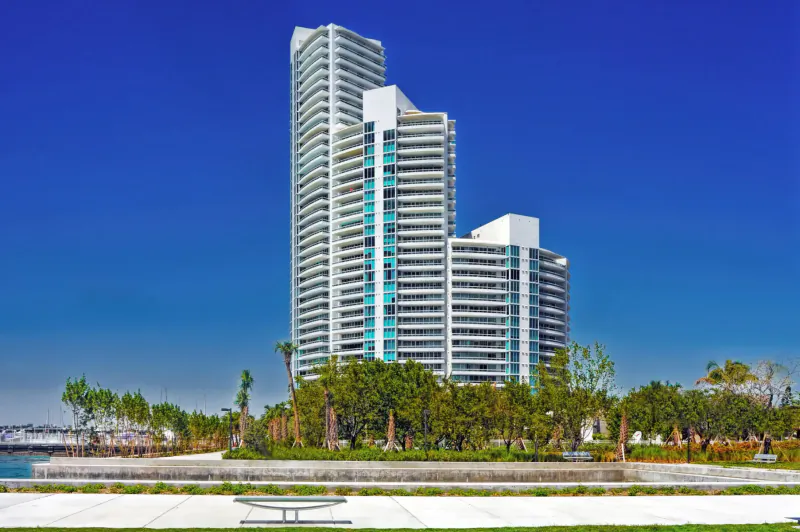 Tall white Murano luxury high-rise towers with palms and waterfront promenade under blue sky