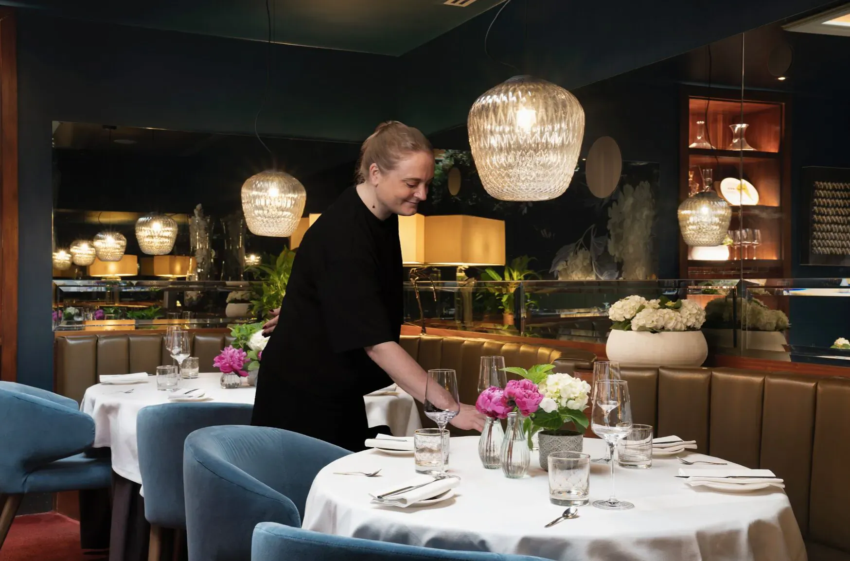 Smiling server in black uniform serving at elegant dining table with pink flowers and teal lamps in Pied à Terre restaurant