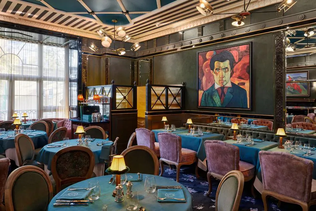 Elegant Kaspia London dining room with teal tables, lamps, and large portrait of man in suit on wall