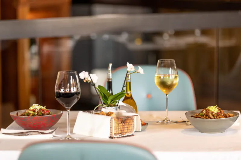 Elegant restaurant table with red and white wine glasses, orchid centerpiece, olive oil, bread basket, and noodle bowls