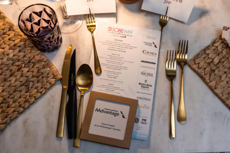 Table set with Delta Sky Club forks, knives, spoons, Scorewife menu, and Management card at outdoor BBQ event.