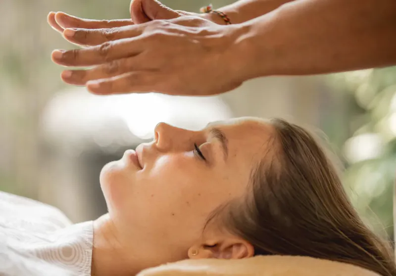 Close-up of hands performing Reiki healing over a relaxed young woman's face at Spring Spa Canggu Bali